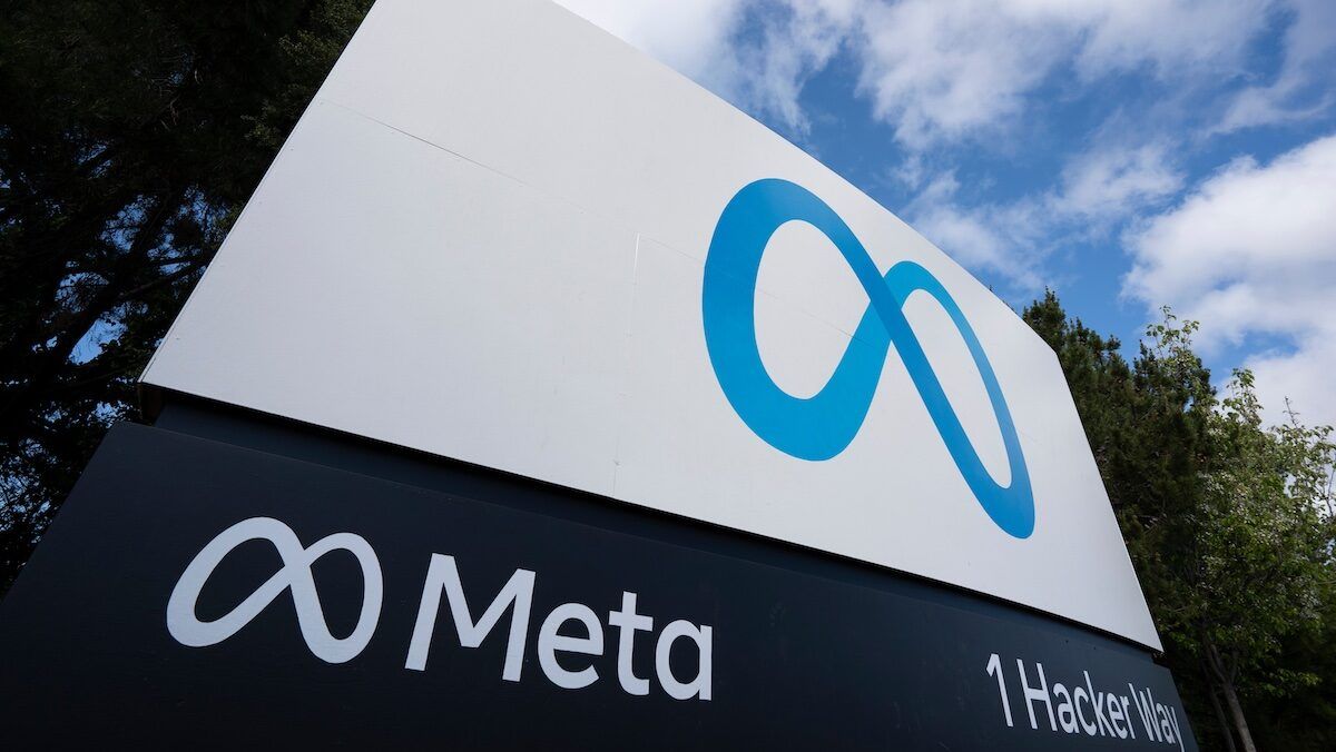 Cartel de Meta con el logo del infinito azul y la dirección 1 Hacker Way, frente a la sede de la empresa, bajo un cielo con nubes