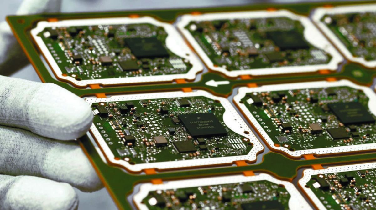 Mano con guante blanco sostiene una placa verde con varias tarjetas electrónicas que llevan chips y componentes soldados
