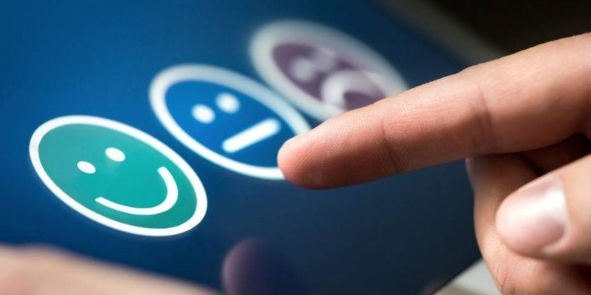 Dedo índice a punto de tocar una pantalla táctil que muestra tres caritas de satisfacción: una verde sonriente, una azul neutra y una violeta triste