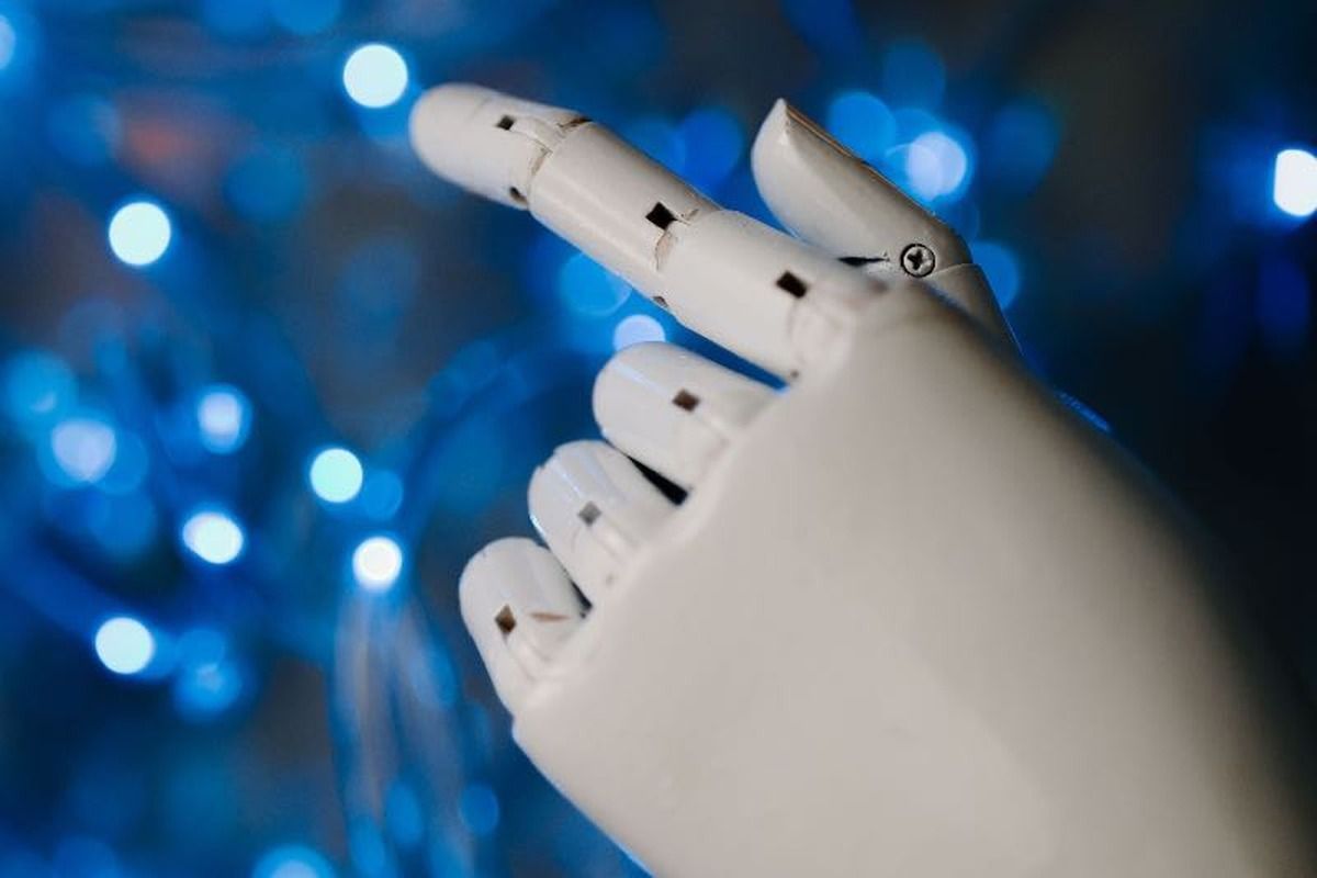 Mano de un robot blanco con los dedos extendidos sobre un fondo azul de luces desenfocadas