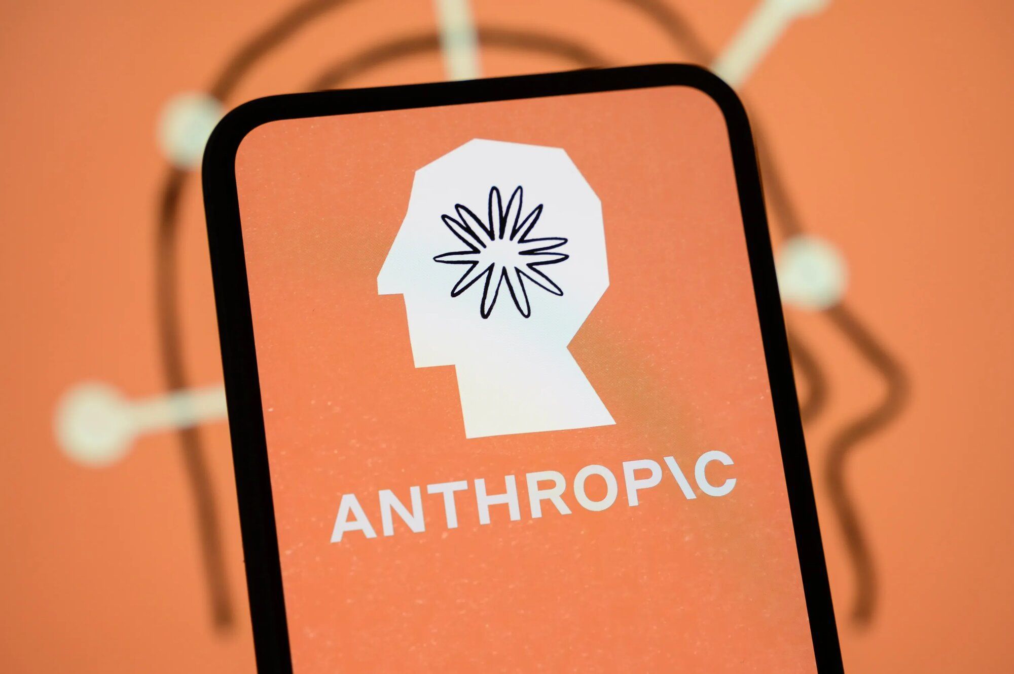 Pantalla de un celular con el logotipo de Anthropic sobre fondo naranja, con la marca de la empresa desenfocada detrás