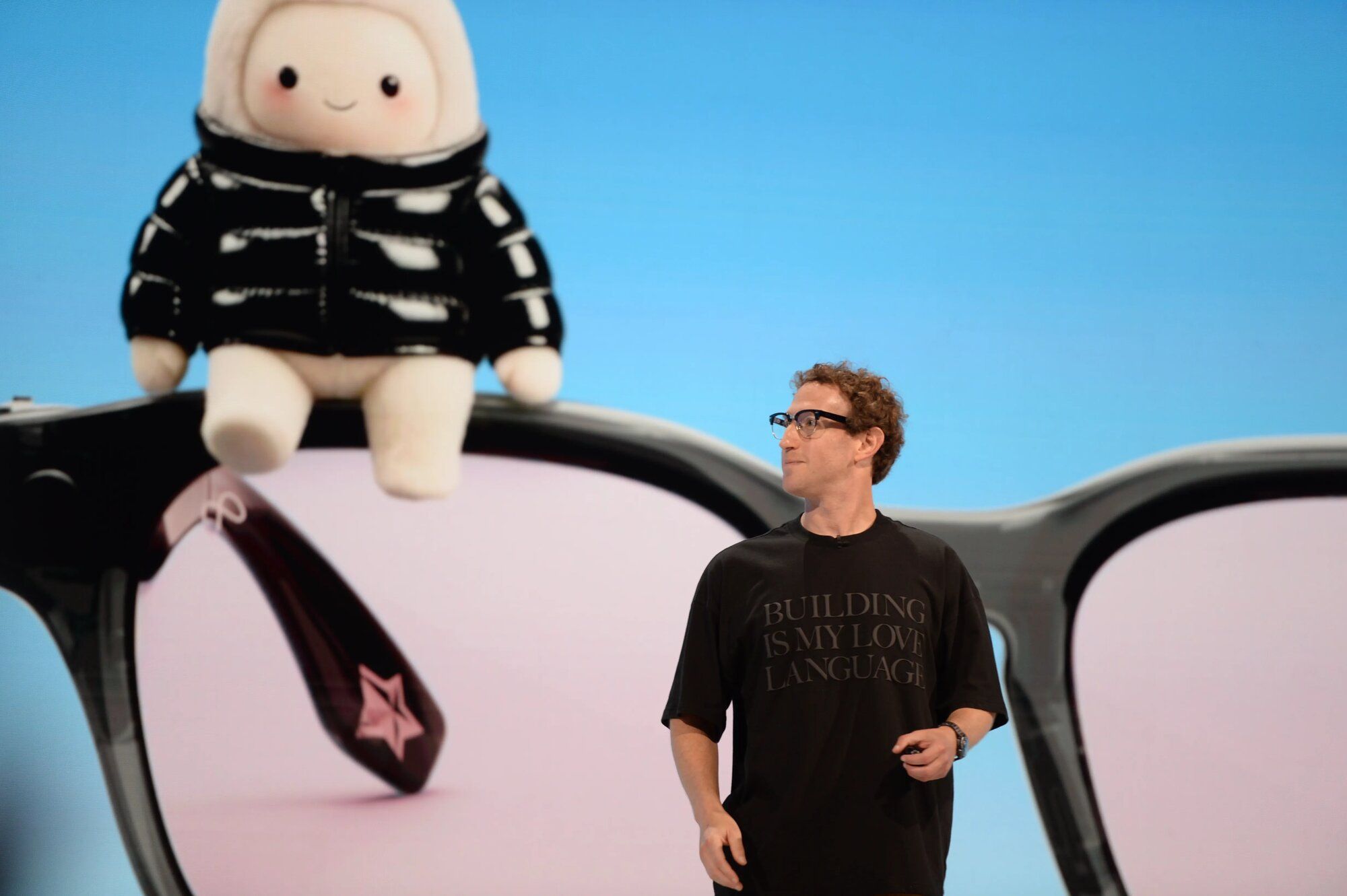 Mark Zuckerberg, director ejecutivo de Meta, en un escenario frente a una pantalla con unos anteojos gigantes y la mascota del asistente Muse