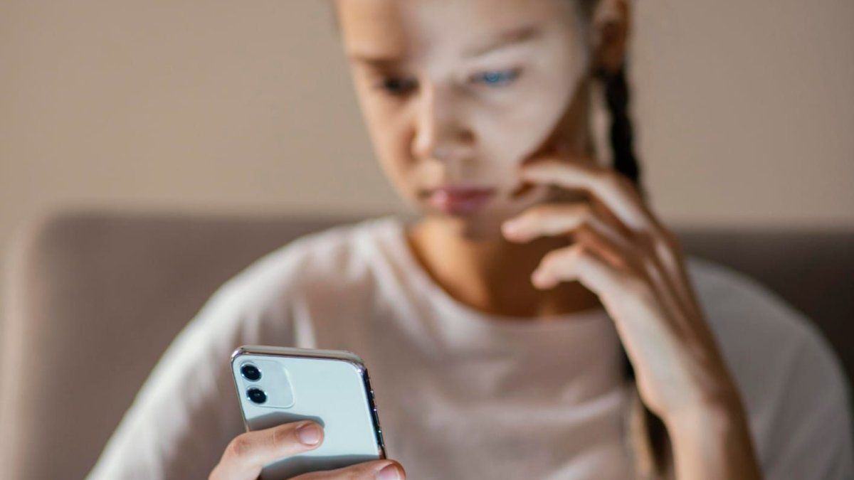 Primer plano de una adolescente de expresión seria que mira la pantalla de un celular que sostiene en la mano