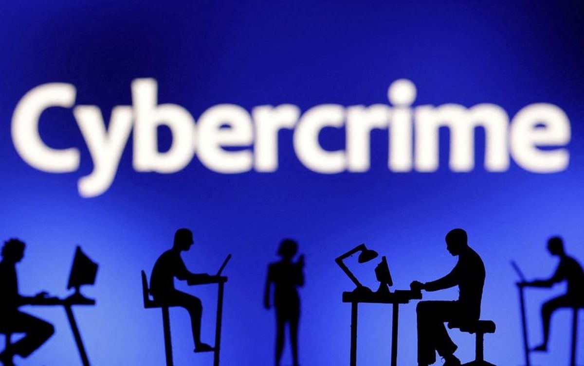 Siluetas de figuras de personas frente a computadoras y celulares, delante de la palabra Cybercrime sobre un fondo azul