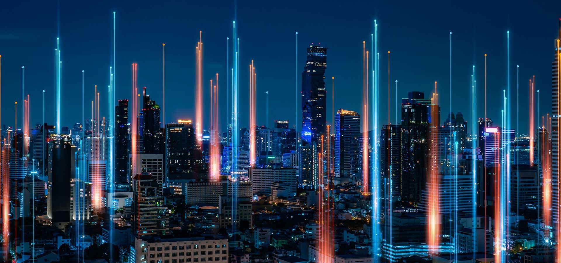 Vista nocturna de una ciudad con rascacielos atravesados por líneas de luz azules y naranjas que simulan conexiones de red