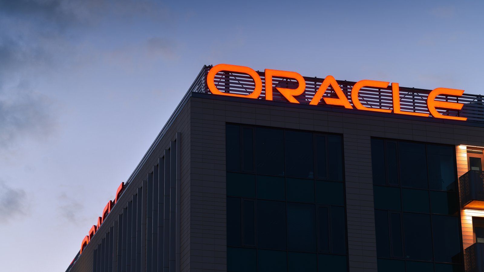 Edificio de oficinas con el logo de Oracle iluminado en naranja sobre la azotea, al atardecer