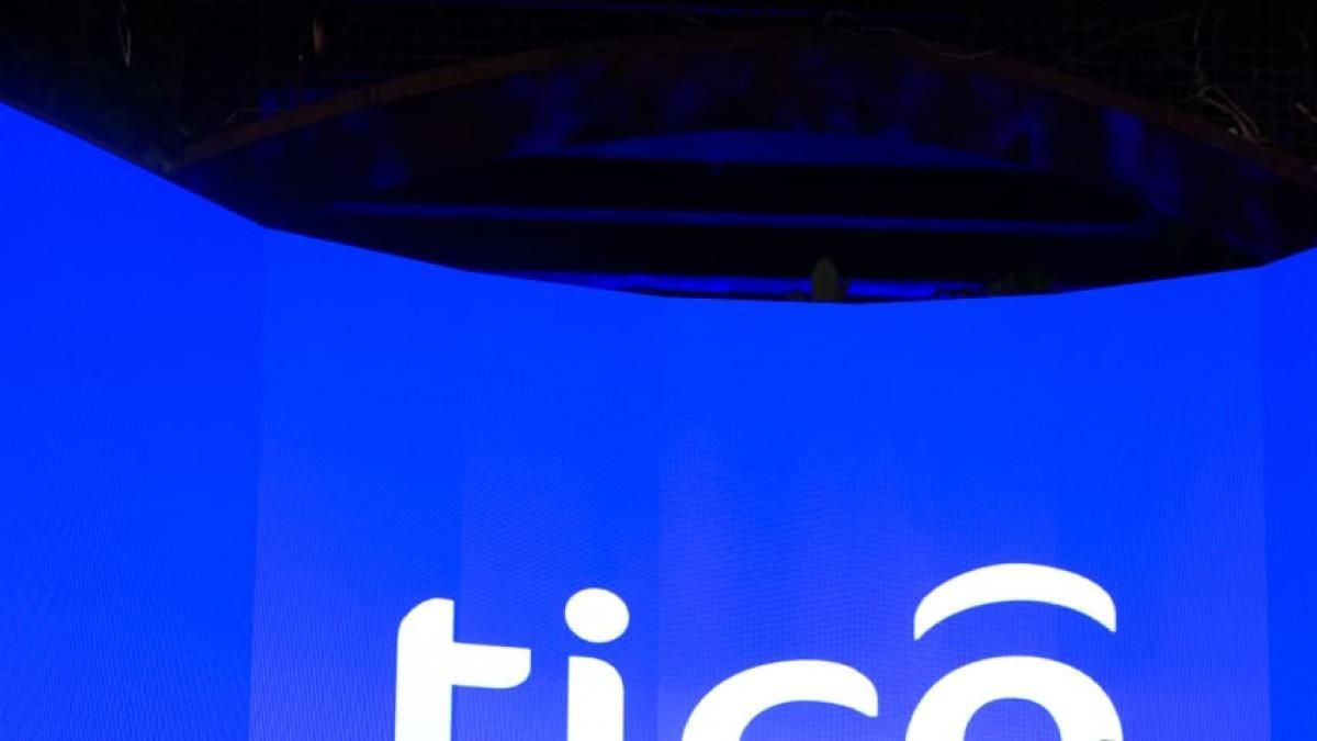 Fondo azul eléctrico iluminado en una escena nocturna, con una estructura oscura curva en la parte superior. En la parte inferior se lee parcialmente el logotipo blanco de Tigo, con letras redondeadas y una curva sobre la o.
